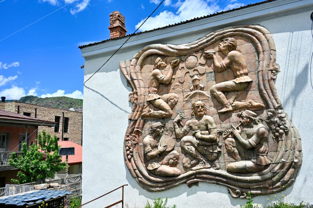 A large stone mural on side of building, carved with pictures of men playing instruments and holding bowls up to the sun.