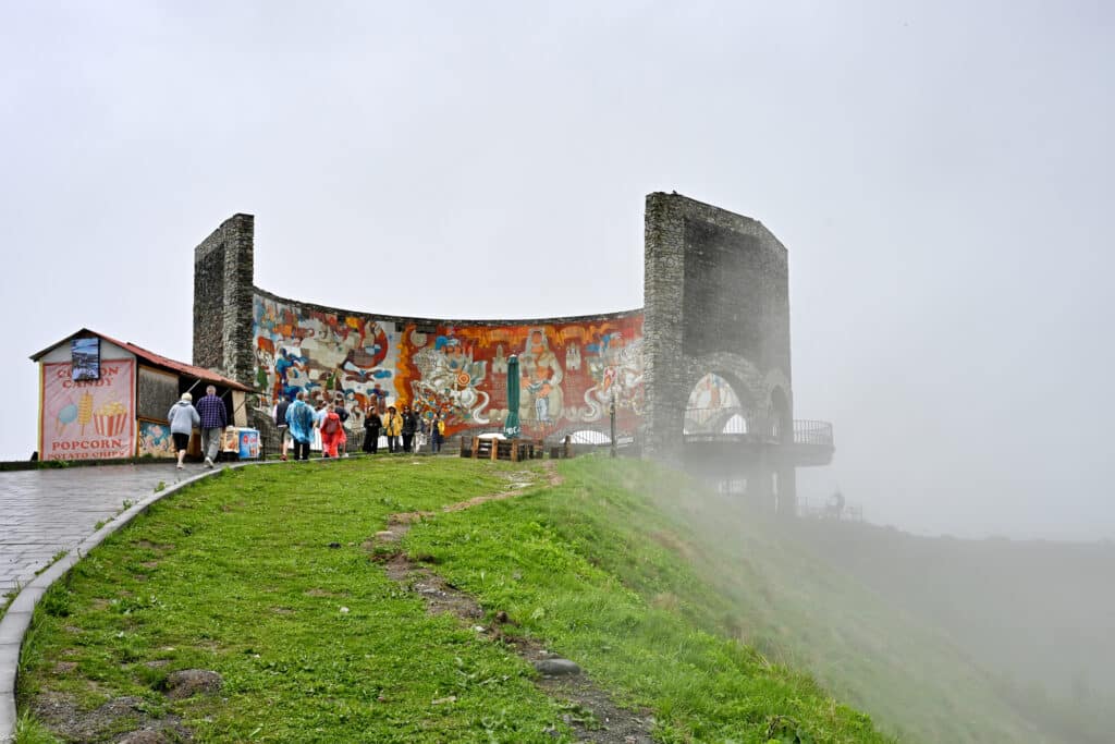 View through the mist to a curved stone sculpture on top of a hill - painted murals on the inside of concrete structure.