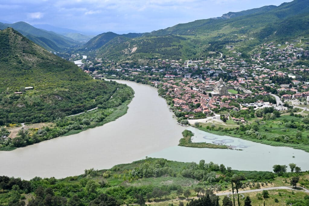 Looking down on the confluence of river - brown river to the left and blue river to the right. Town on the river banks. Green hills.