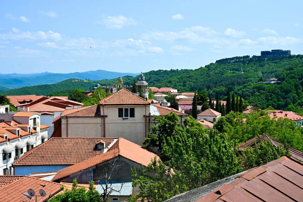 View over terracotta roods to green hillsides beyond. Pale blue sky above.