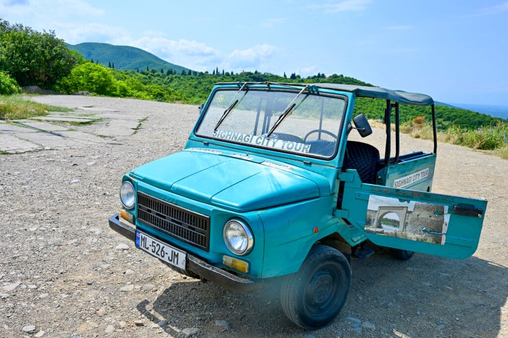 A small turquoise blue jeep stands with door open advertising Sighnai City Tour.
