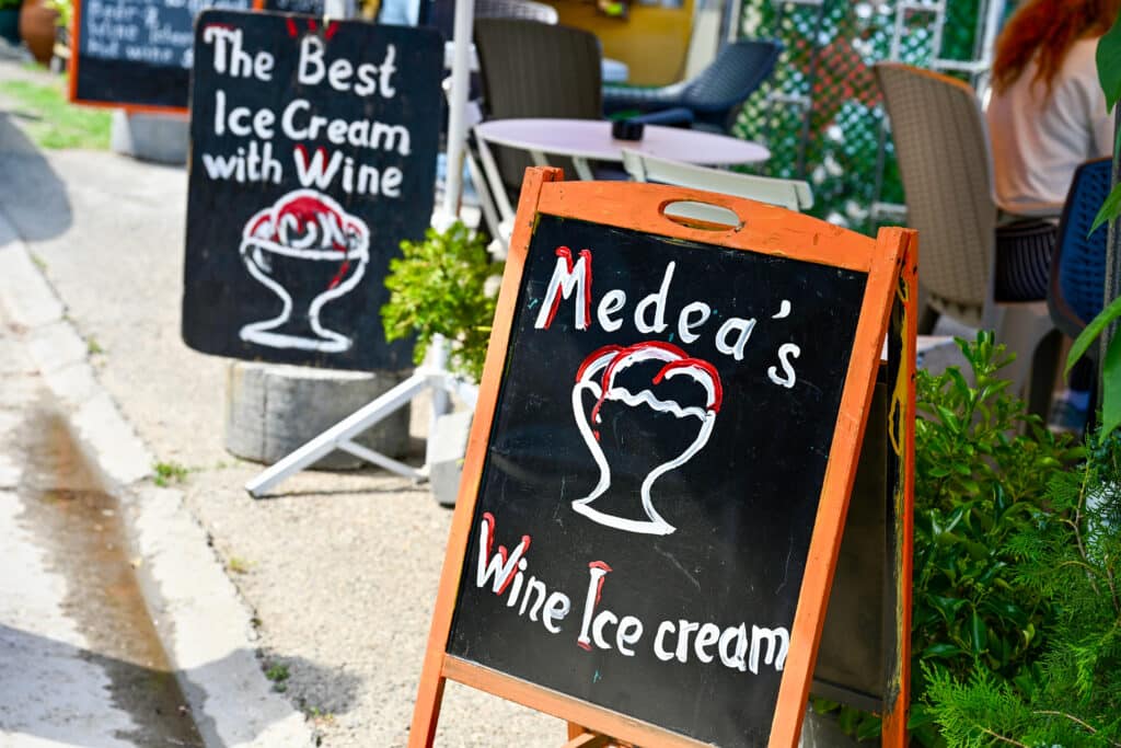 Wooden sign advertising Medea's Wine Ice Cream. A second sign behind advertises The Best Ice Cream with Wine. Cafe tables to the right