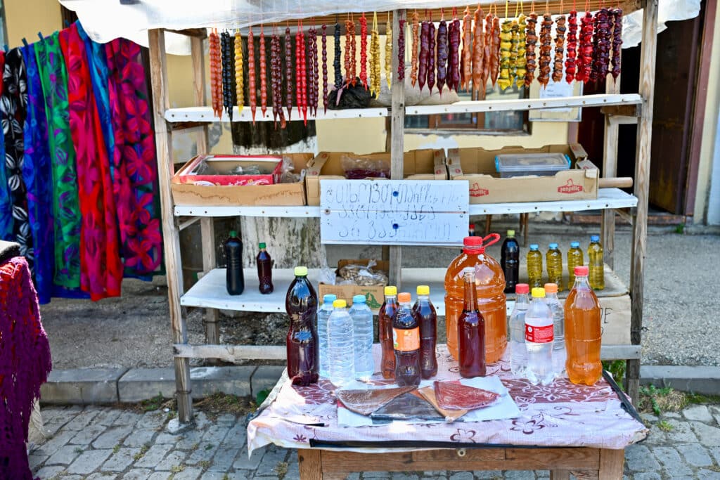Market stall of hanging strings of food. Bottles of home made brew in front