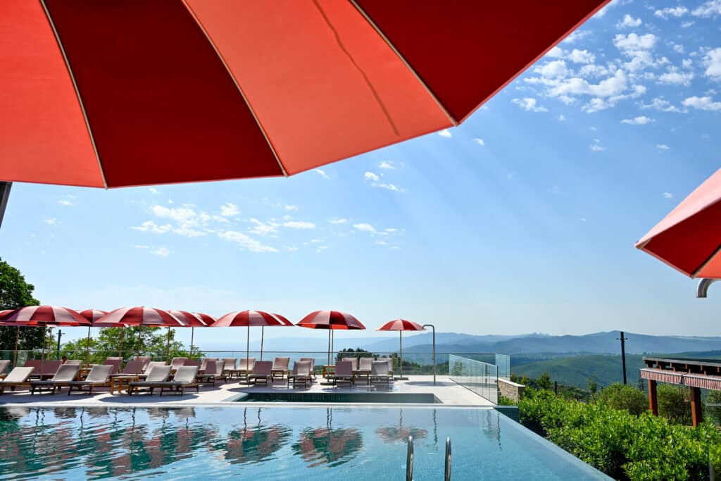 Row of pink and burgundy sun parasols around a swimming pool. One umbrella overhead