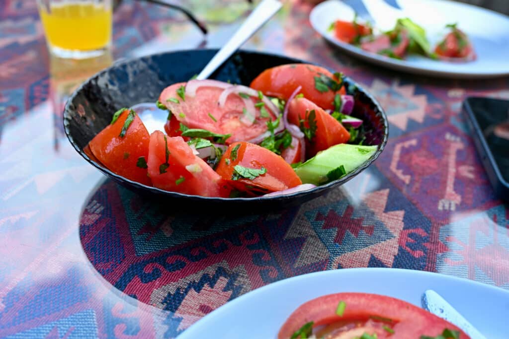 Black bowl filled with tomato salad sits on lunch table.