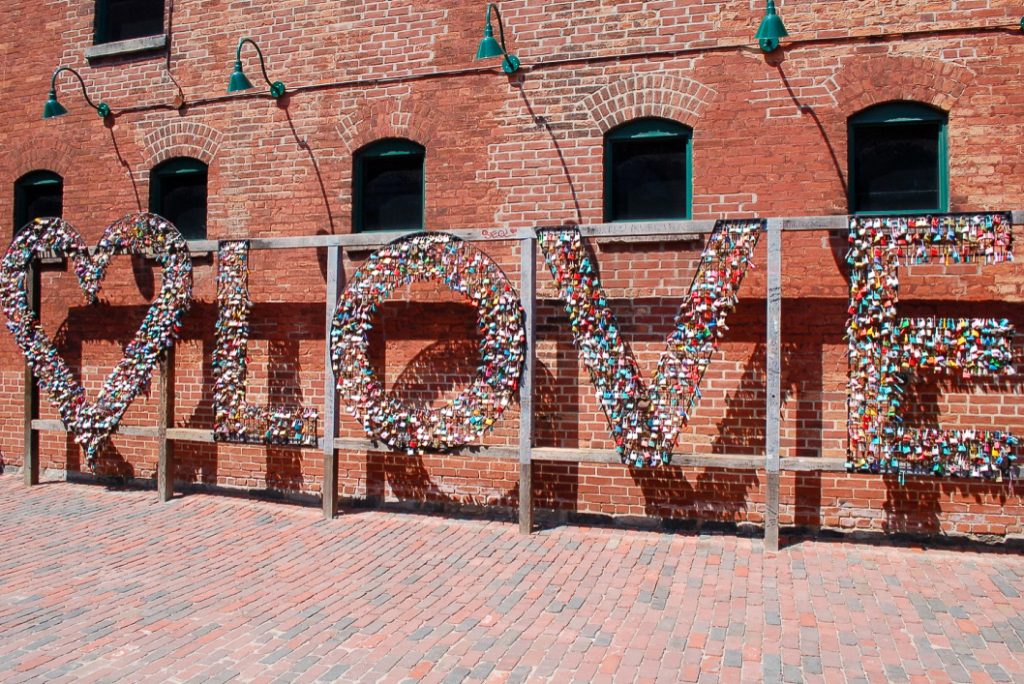 Letters spelling LOVE covered in padlocks in front of brick wall
