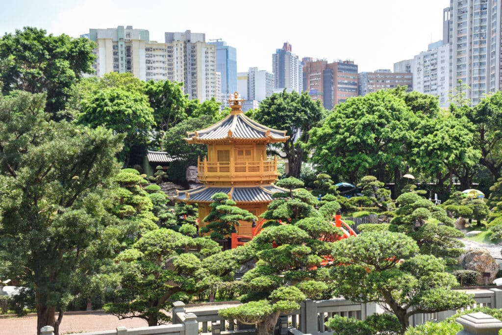 Small orange pagoda surrounded by trees. Skyscrapers behind.