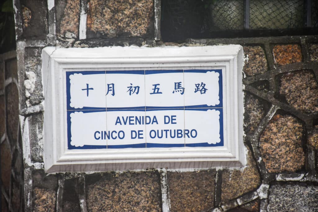 A white road sign with Chinese characters and Portuguese name