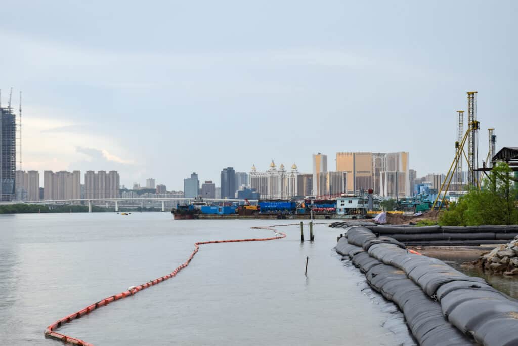 Looking down a still river along riverbank to city buildings on horizon