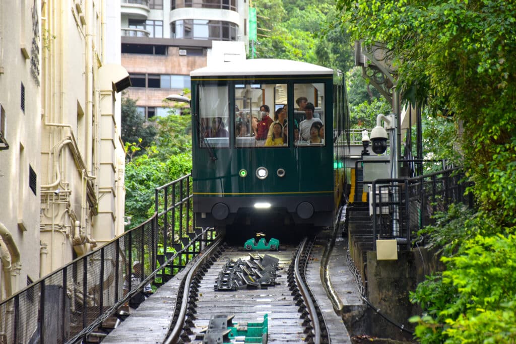 A green tram approaches the camera through buildings and trees