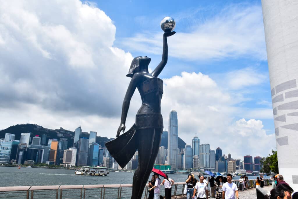 Tall sculpture of a lady holding silver ball to the sky, Cityscape behind across water