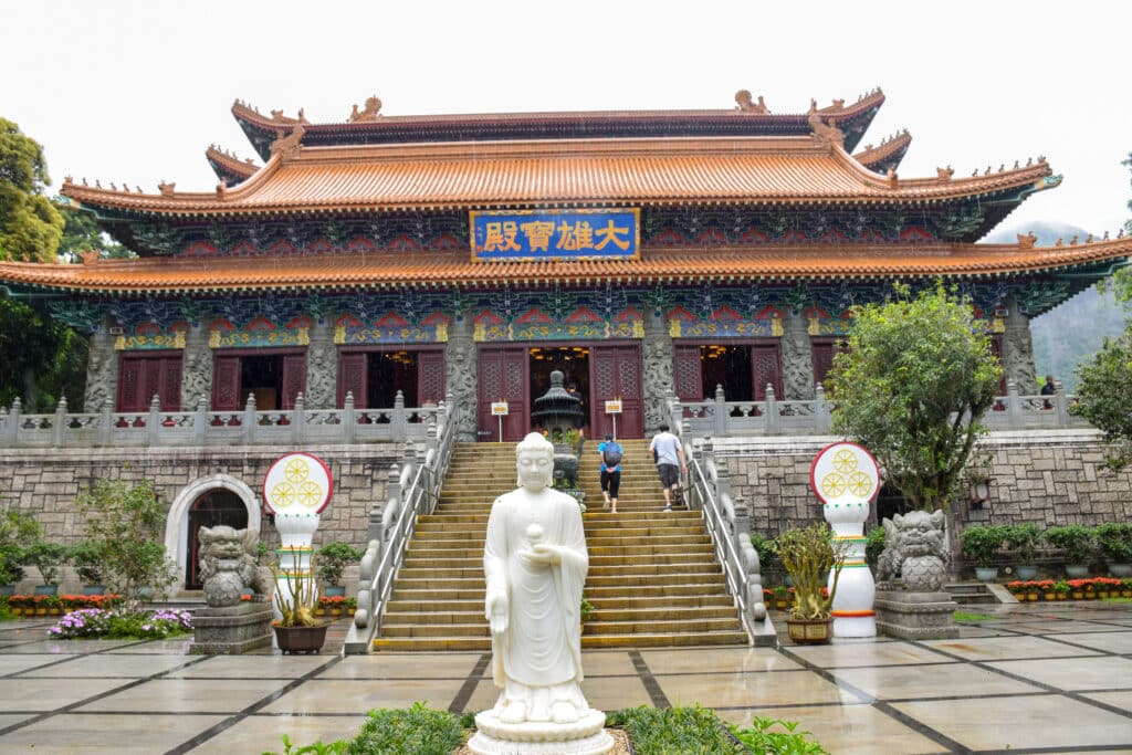 Large Chinese monastery building with pagoda style roof. White statue in foreground