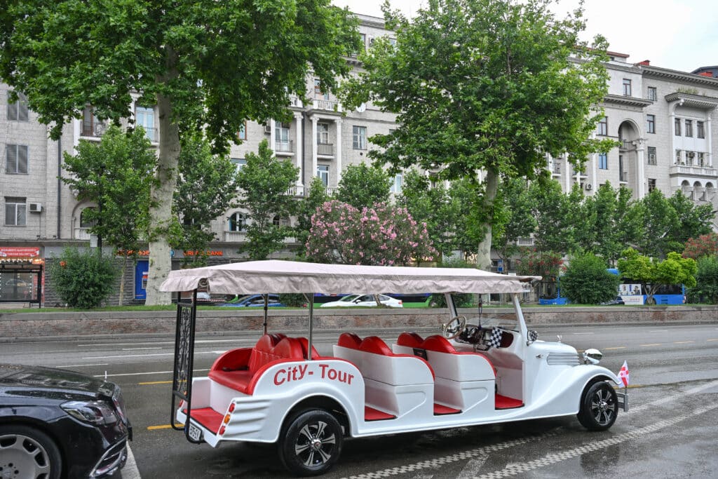 White golf buggy advertising City Tour sits empty on road with trees behind.
