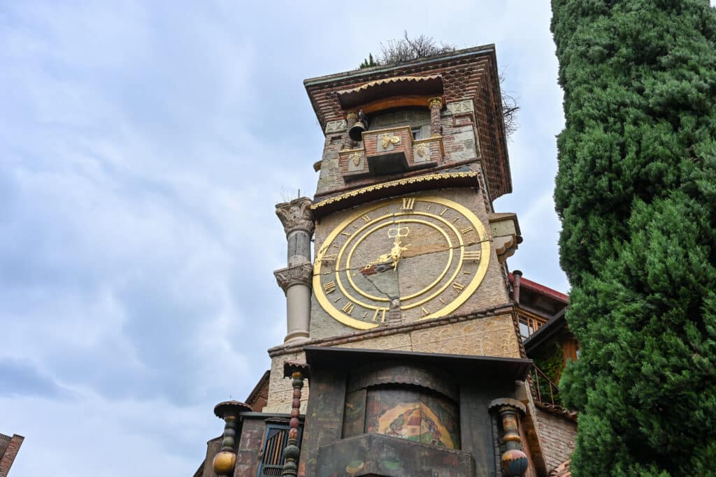 Looking up at the top of a crooked tower with clock face on front.