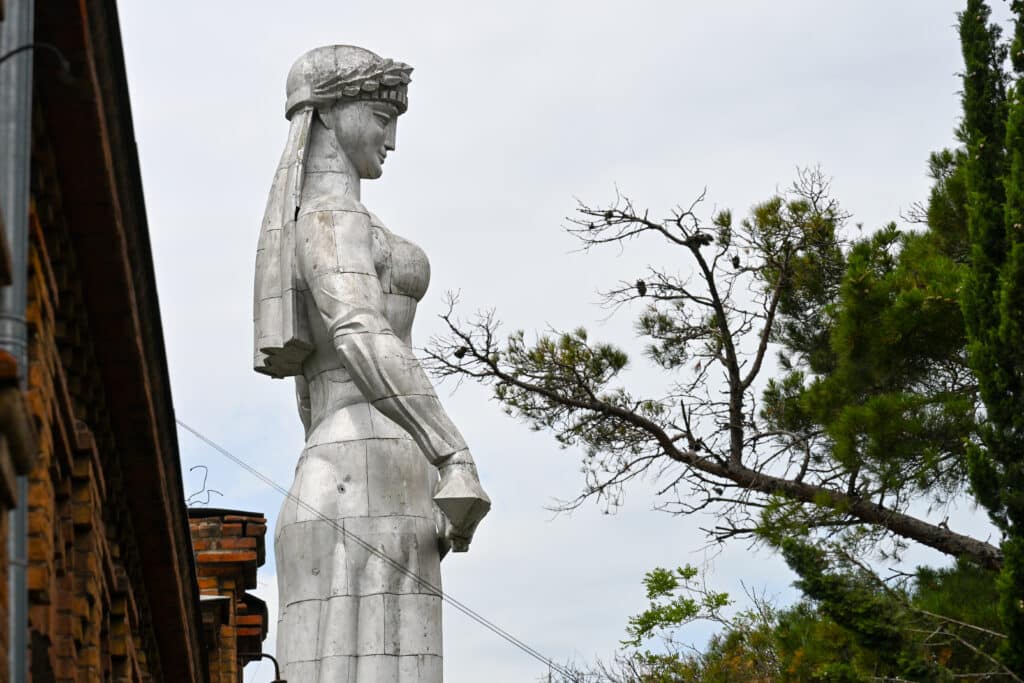 A silver aluminium statue of lady looks to the right.