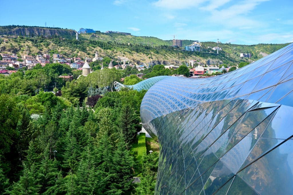 Modern glass structure snakes through trees to a town on horizon