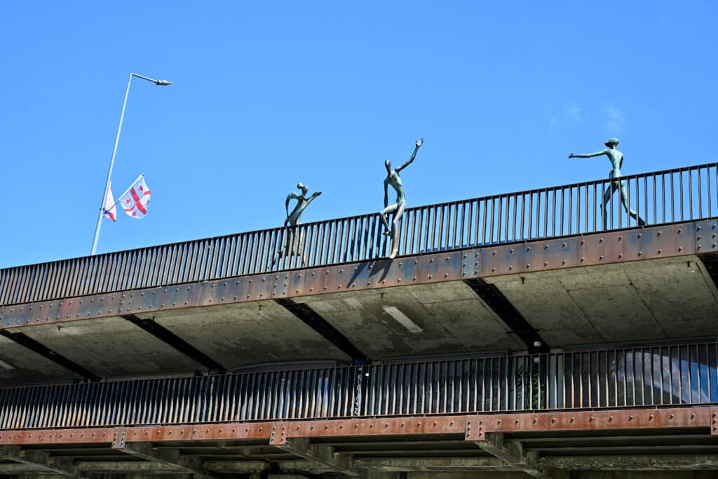Looking up at 3 metal statues of people on bridge