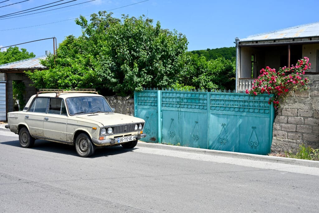 Old fashioned cream car to the left of turquoise house gates. Tree behind