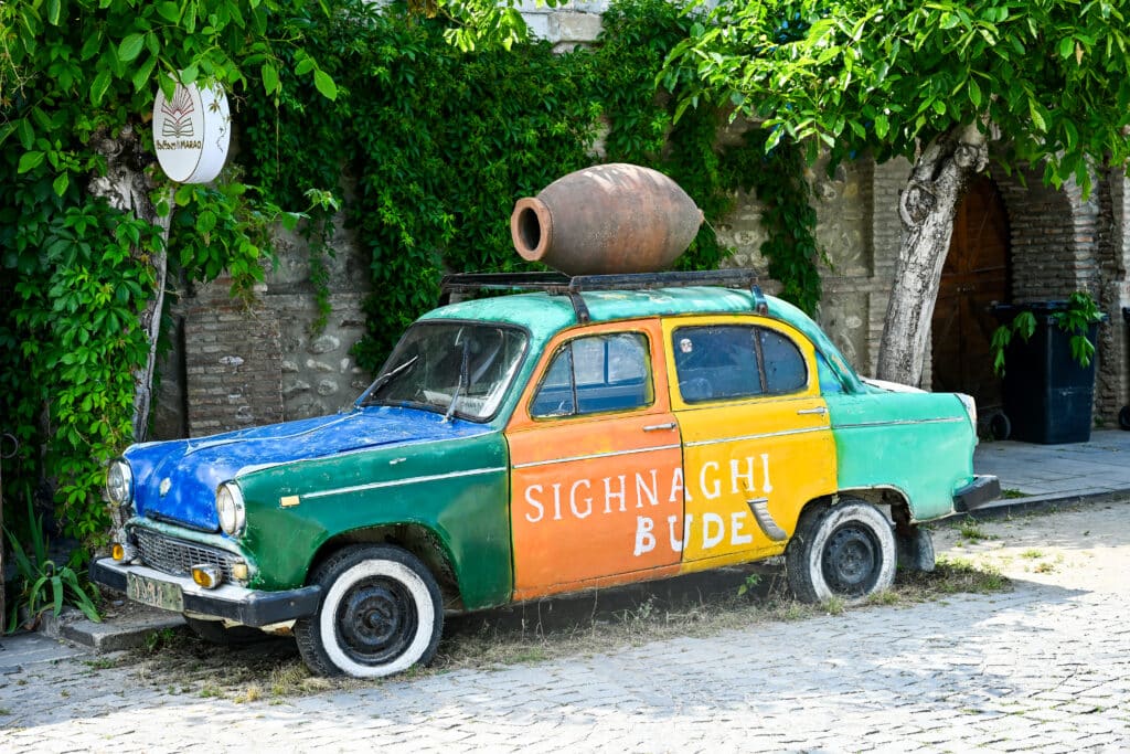 Old painted car with clay vessel on its roof. Says Sighnaghi on side