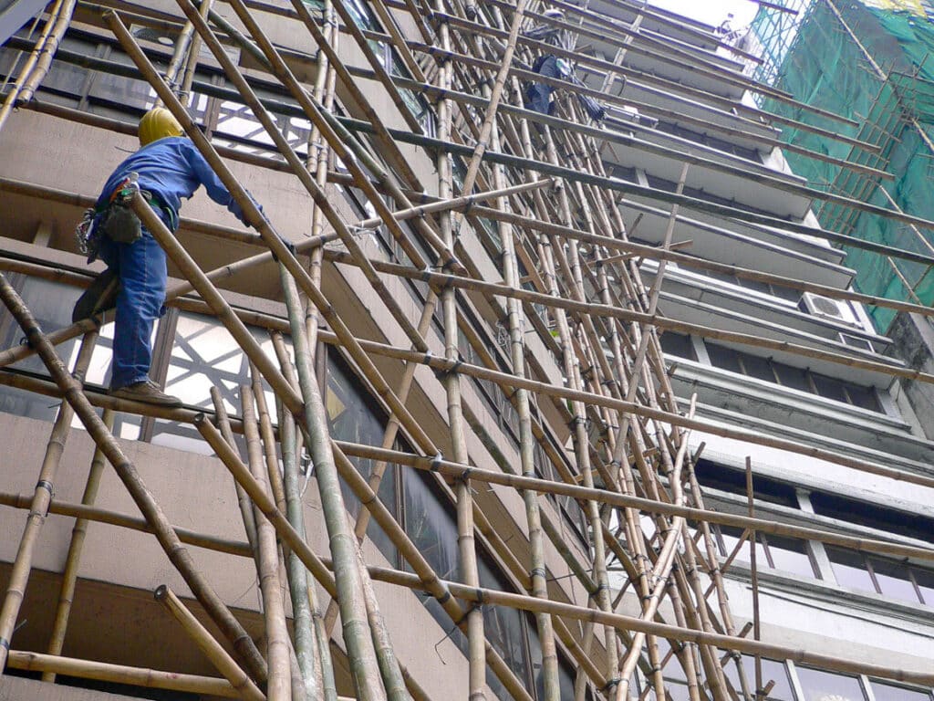 Looking up at tall old building with bamboo scaffolding in front and workers on the scaffolding