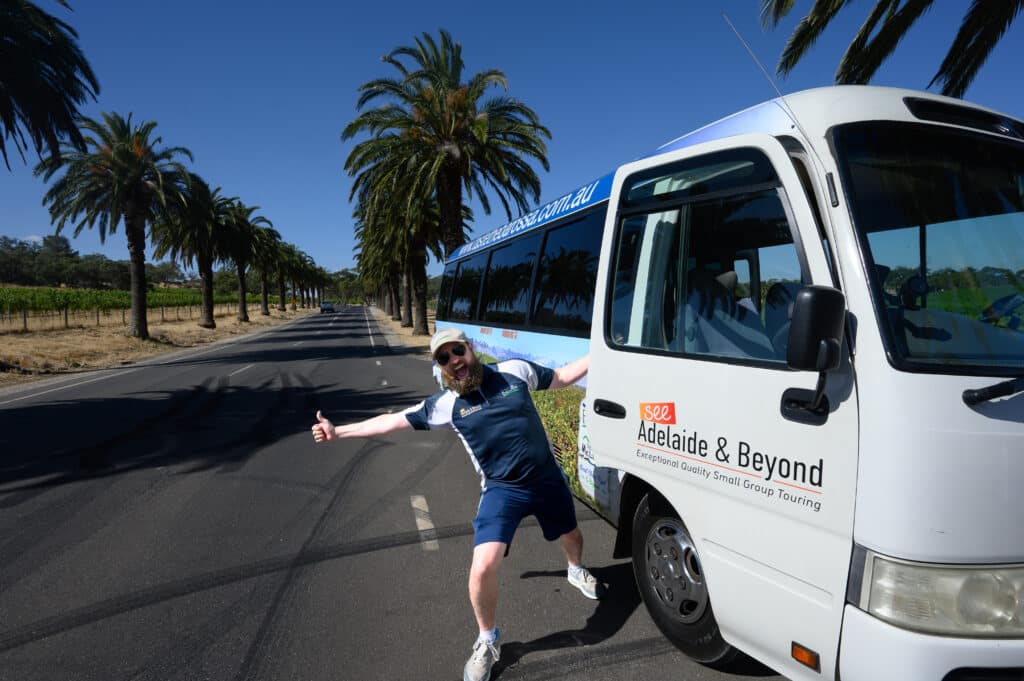 Barossa Valley tour guide posing next to bus on palm road