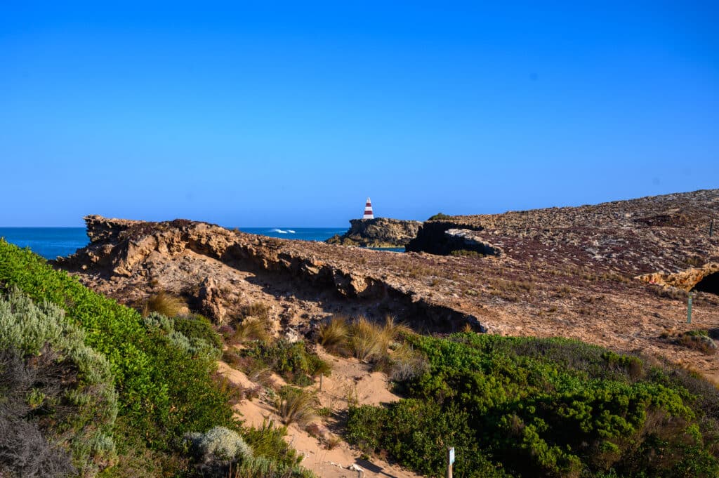 Red-and-white Robe Obelisk stands on a rocky promontory above eroded limestone cliffs and coastal vegetation.