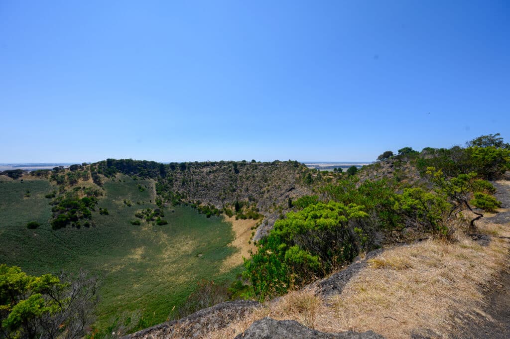 Expansive view across the green and brown crater of Mount Schank from the rocky rim path.