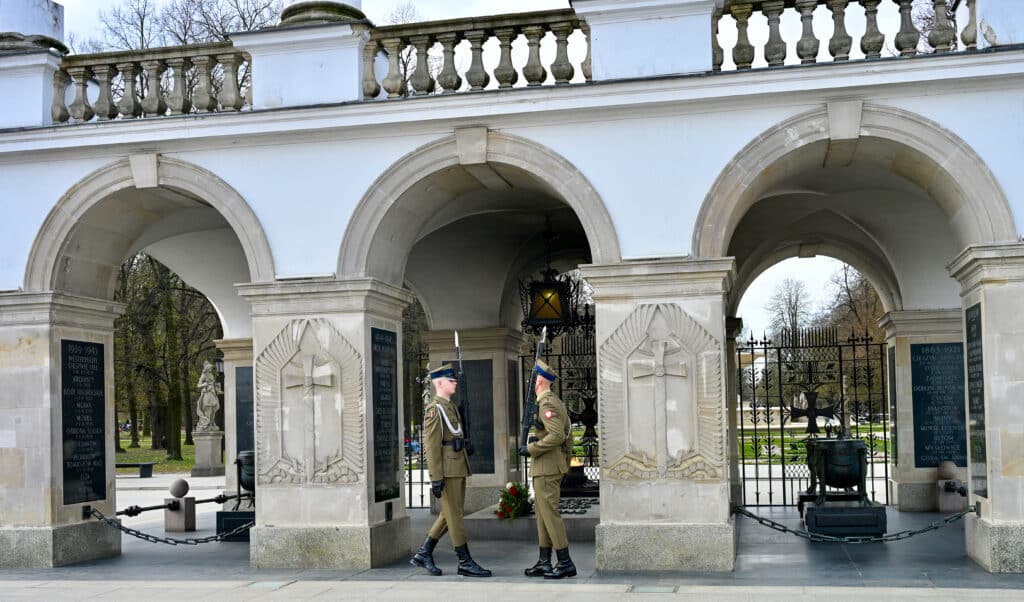 Two soldiers in green uniforms meet in front of an arch