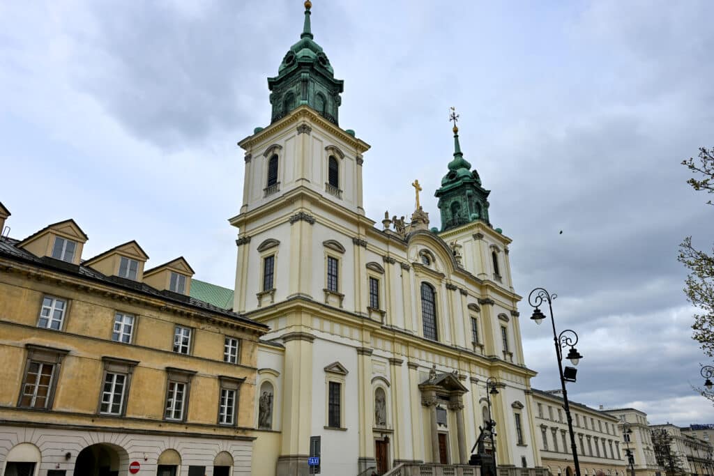 Cream stone Baroque church with two green towers in row of buildings