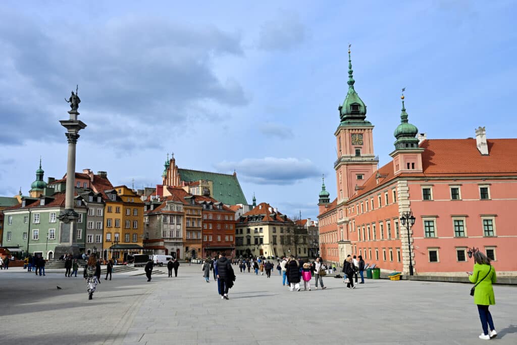 Large red brick palace behind tall column with statue on top in middle of square