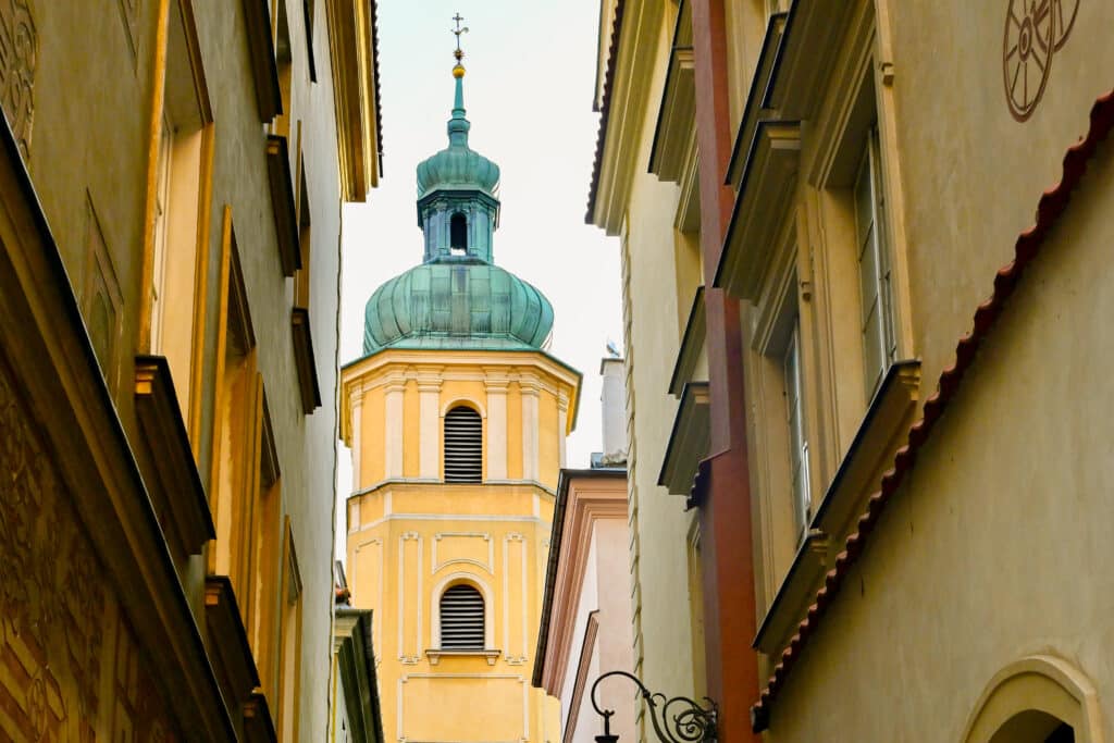 A pretty yellow square stone tower with copper domed top appears between two rows of buildings
