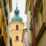A pretty yellow square stone tower with copper domed top appears between two rows of buildings