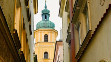 A pretty yellow square stone tower with copper domed top appears between two rows of buildings