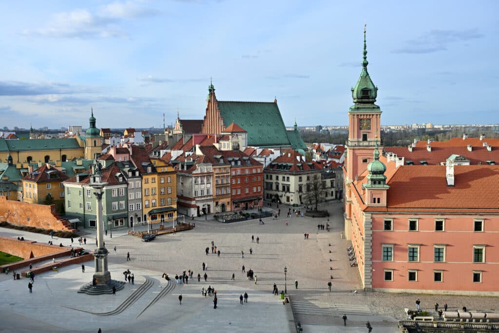 View from on high looking down into an open square with column and palatial looking building. Multicoloured buildings