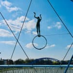 Metal acrobat sculpture on river bridge