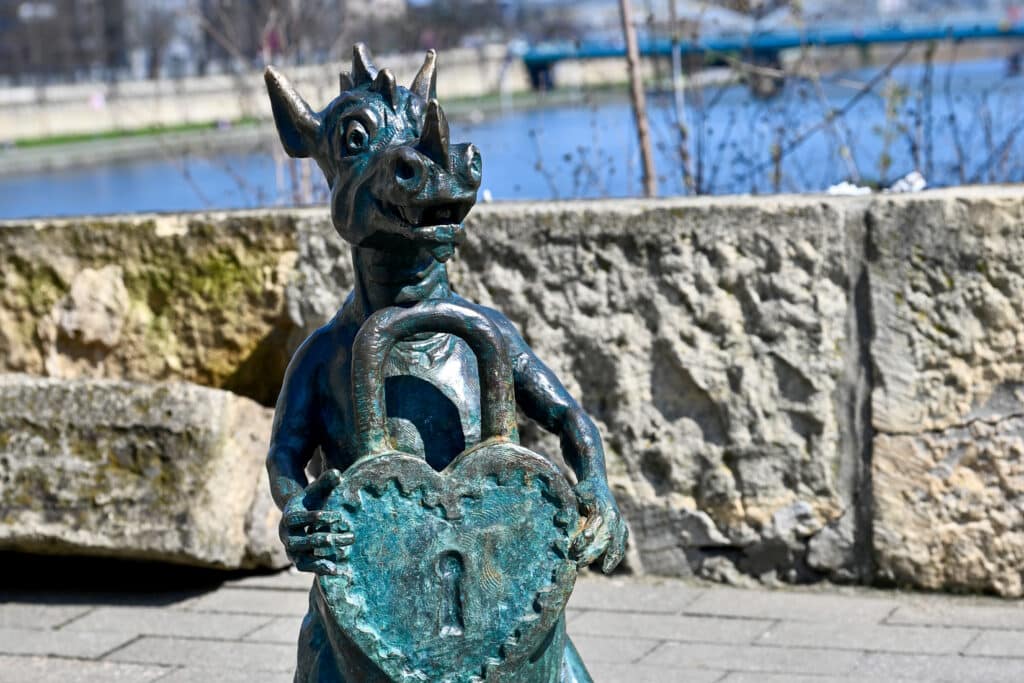 Statue of a dragon holding a heart shaped padlock in front of river
