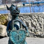 Statue of a dragon holding a heart shaped padlock in front of river
