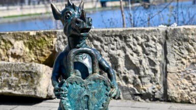 Statue of a dragon holding a heart shaped padlock in front of river