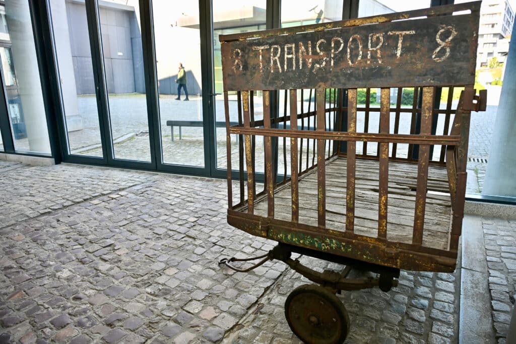 Old metal cart or trolley parked on cobblestones in museum building. It says Transport 8 on the trolley