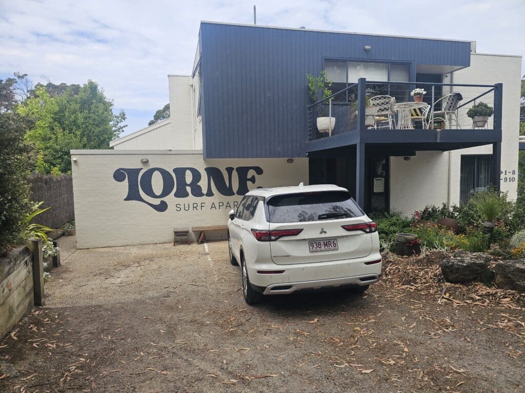 Lorne Surf Apartments exterior with blue cladding, white brickwork, a furnished balcony and a white SUV parked outside.