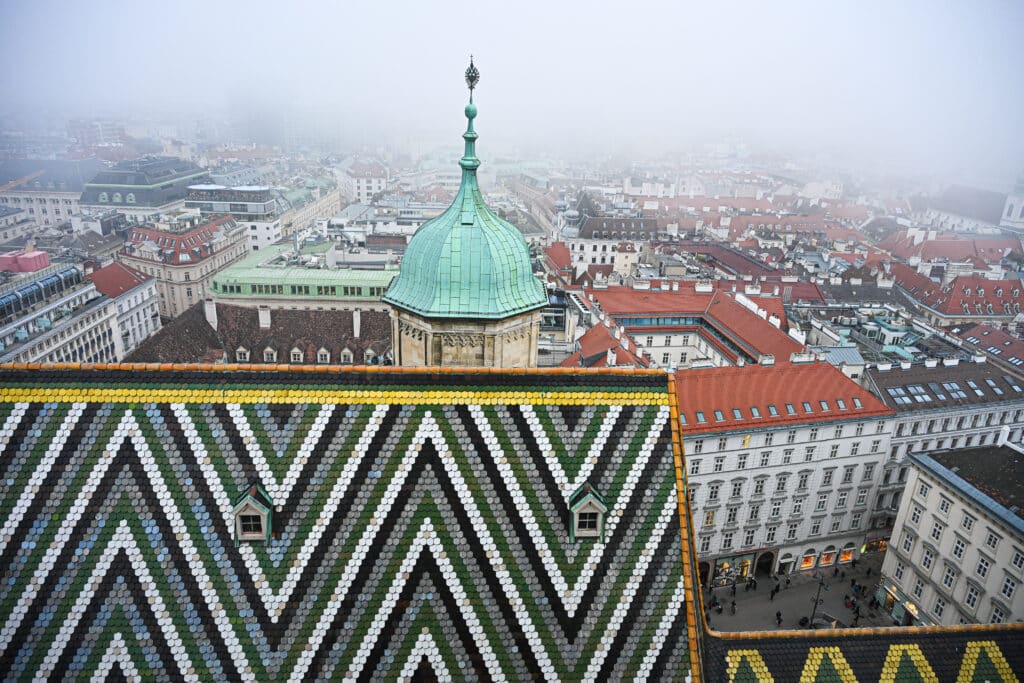 View from an elevated position looking down on town with red roofs. Coloured roof tiles in foreground. Green cupola in middle