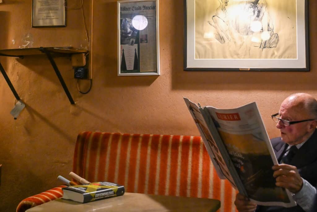 Man sits on a sofa reading newspaper. Paintings on wall in cosy room
