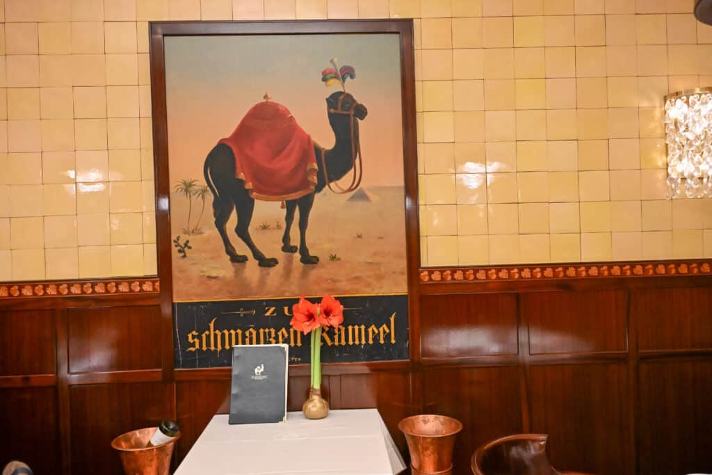 View of a restaurant table with white cloth. Poster of a black camel hangs over the table