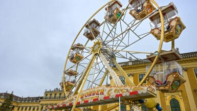 Old fashioned ferris wheel in front of large yellow palace