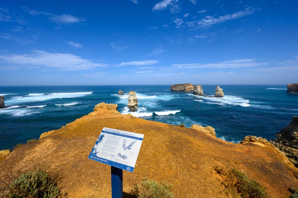 A Kirrae Whurrong interpretation sign overlooks ochre cliffs, limestone stacks and breaking waves at the Bay of Islands.