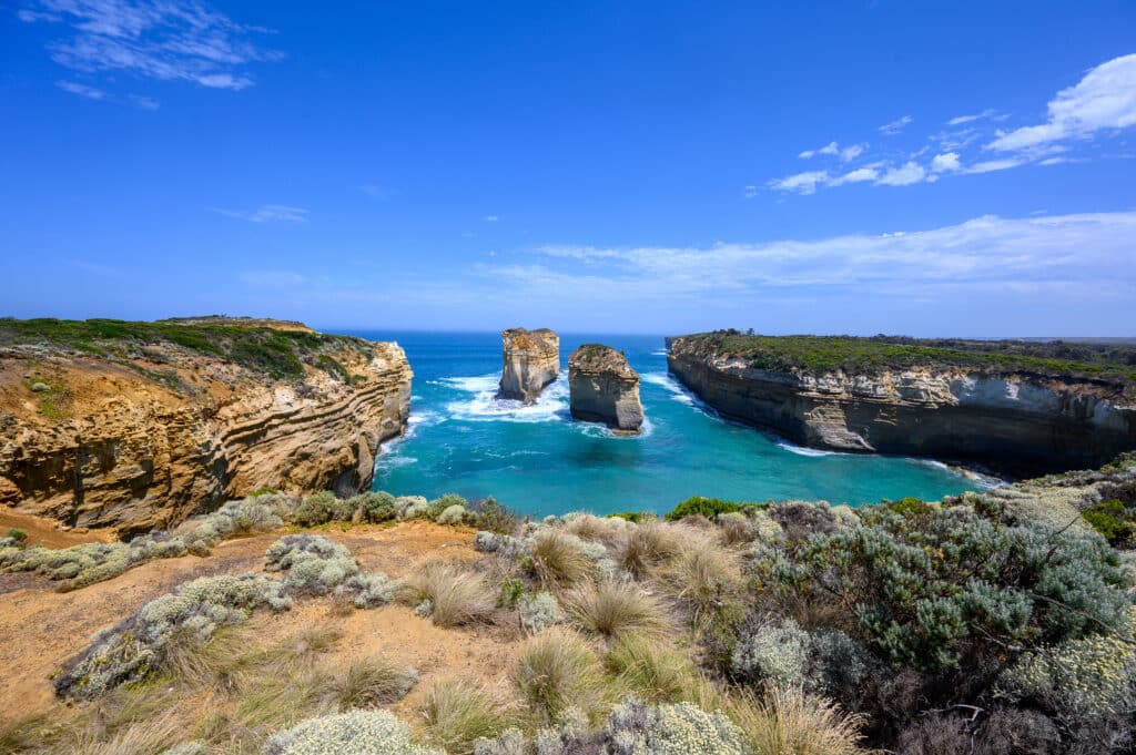 The Tom and Eva limestone stacks stand in turquoise water between steep cliffs near Loch Ard Gorge, Victoria.