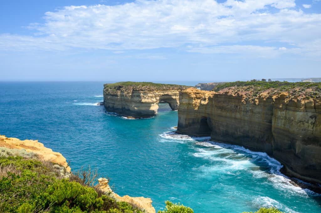 An arch-shaped opening in Mutton Bird Island rises above turquoise water beside the sheer cliffs near Loch Ard Gorge.