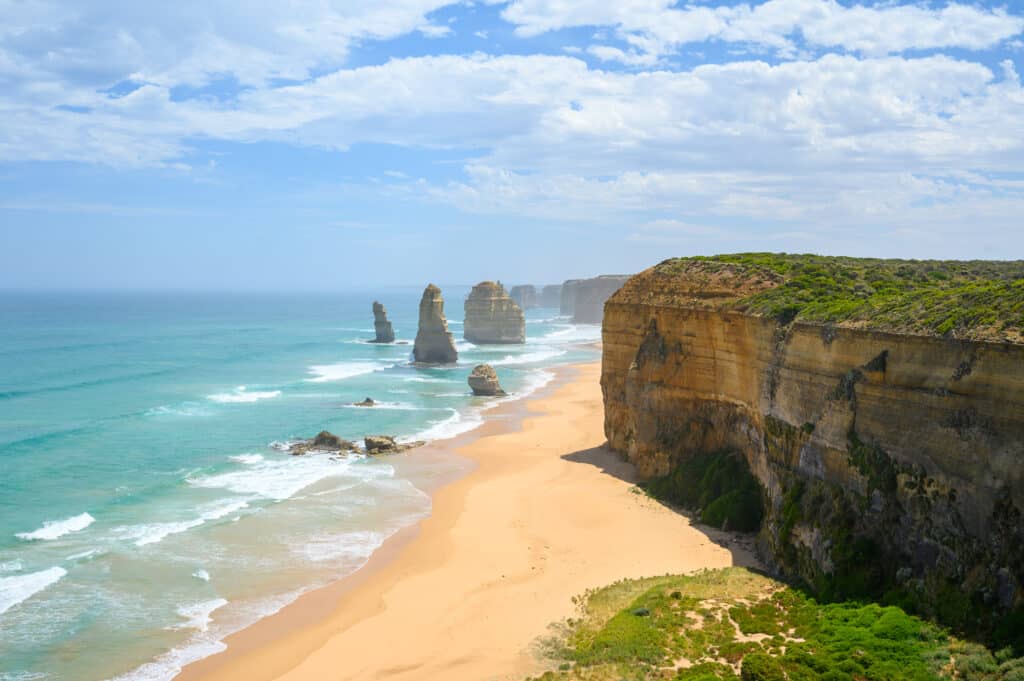 Twelve Apostles limestone stacks rise from turquoise surf beside a golden beach and sheer cliffs on Victoria’s Great Ocean Road.