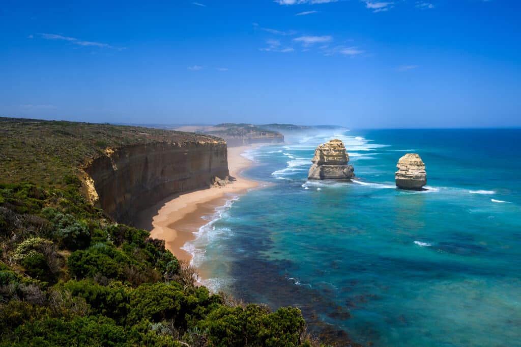 Gog and Magog limestone stacks stand offshore from Gibson Beach, beside high cliffs and turquoise water on Victoria’s coast.