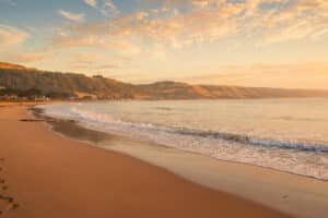 Warm morning light falls across Apollo Bay Beach and the surrounding hills as a small wave breaks along the shore.